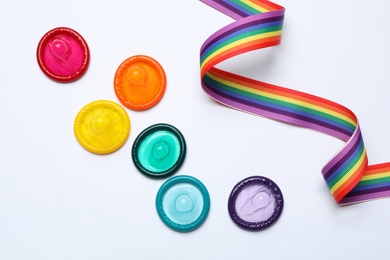 Photo of Colorful condoms and rainbow ribbon on white background, top view. LGBT concept