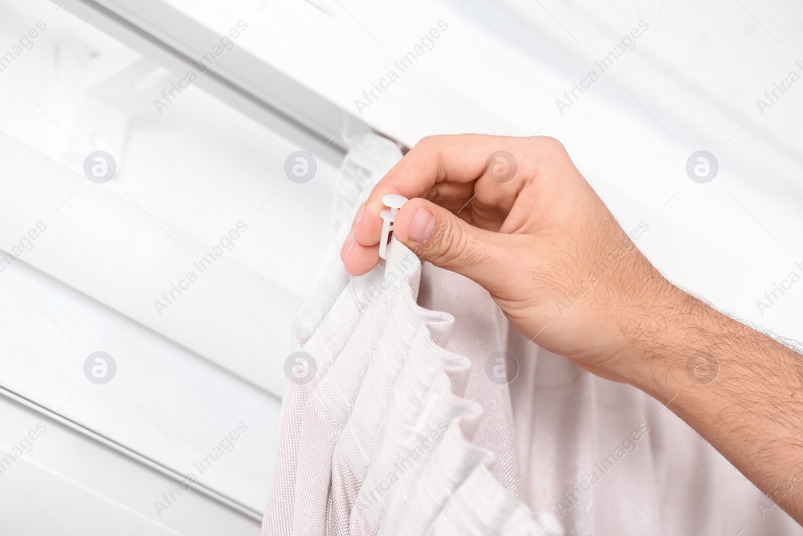 Photo of Young man hanging window curtain in room, closeup