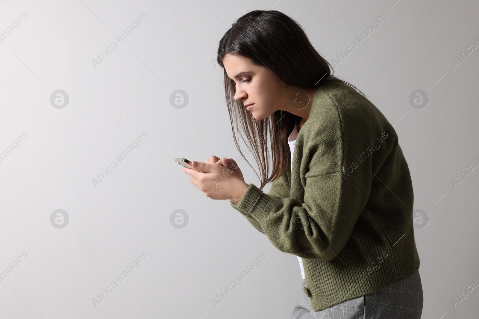 Photo of Young woman with bad posture using smartphone on grey background. Space for text