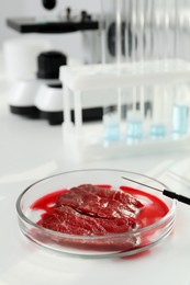 Petri dish with pieces of raw cultured meat on white table in laboratory, space for text