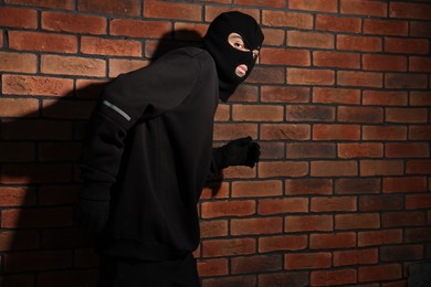 Photo of Thief in balaclava against red brick wall. Space for text