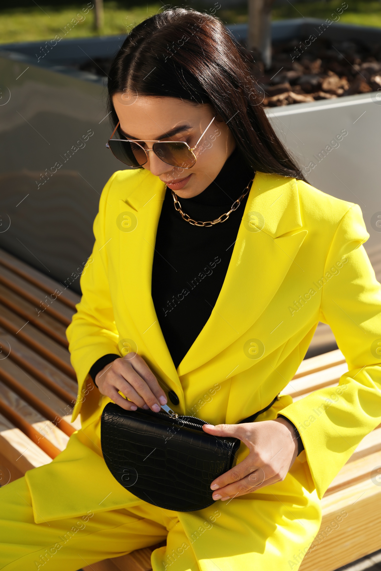 Photo of Beautiful young woman with stylish waist bag sitting on bench outdoors