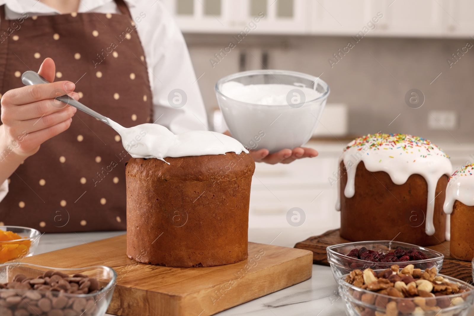 Photo of Woman decorating traditional Easter cake with glaze at white marble table in kitchen, closeup