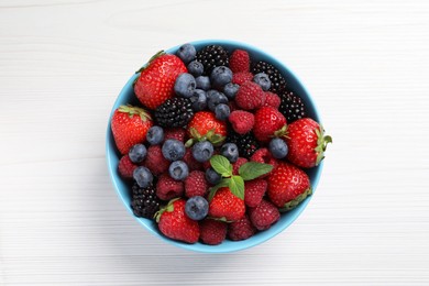 Photo of Many different fresh ripe berries in bowl on white wooden table, top view