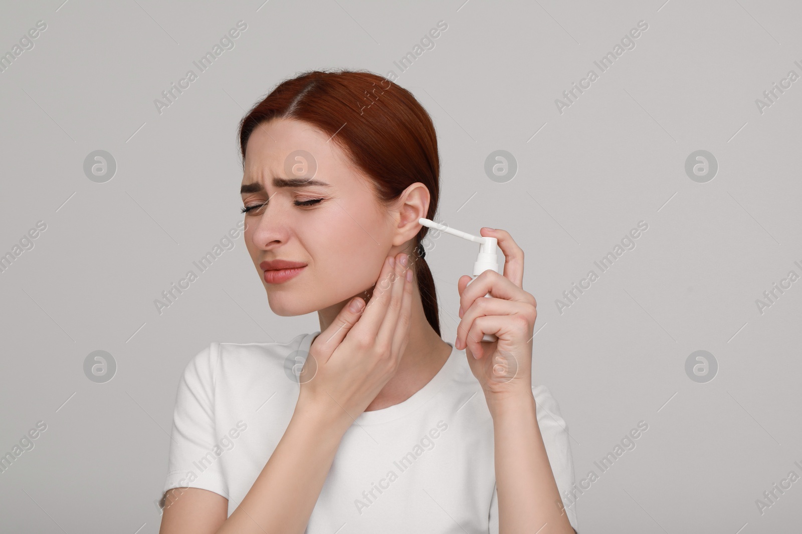 Photo of Unhappy woman using ear spray on light grey background