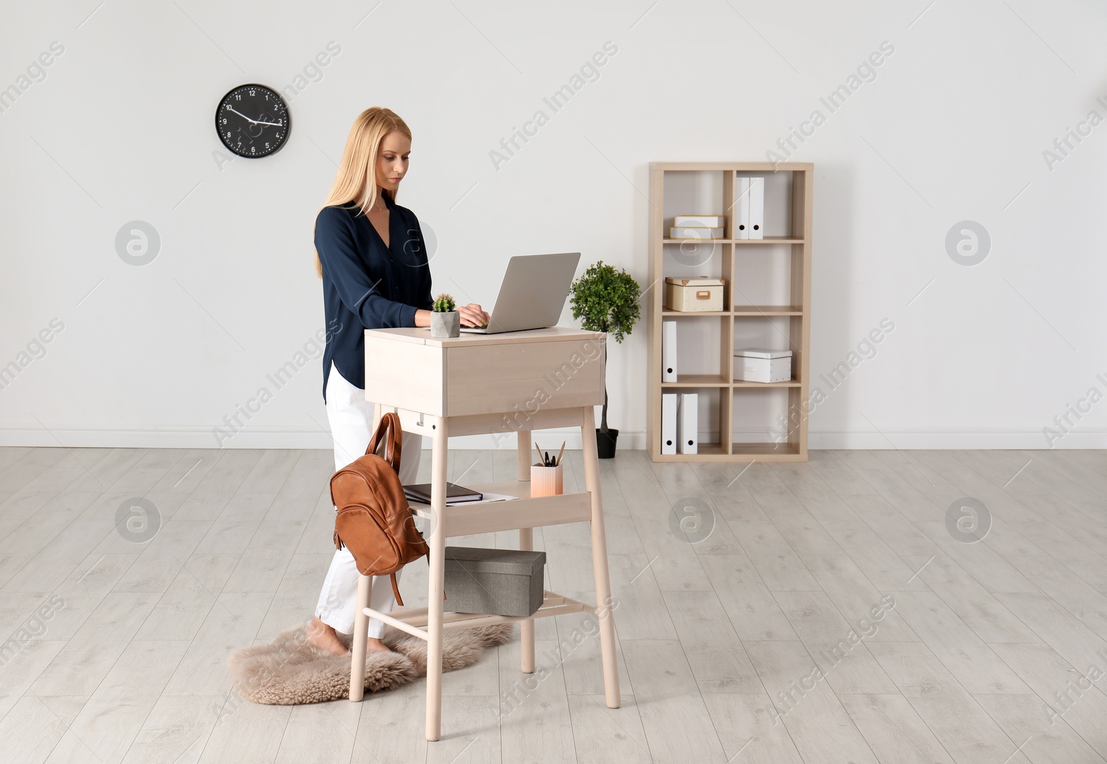 Photo of Young woman using laptop at stand up workplace indoors