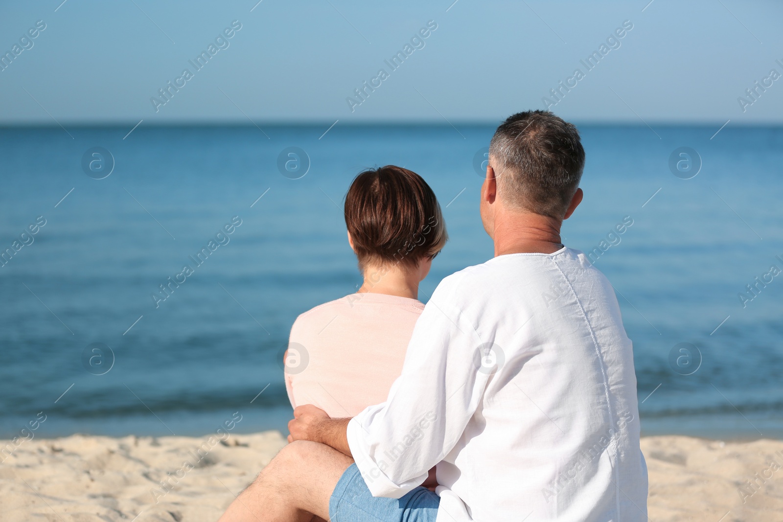 Photo of Happy mature couple sitting together at beach on sunny day