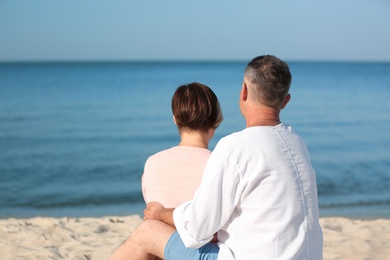 Photo of Happy mature couple sitting together at beach on sunny day