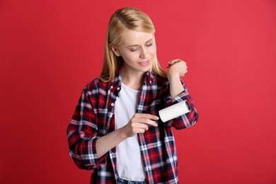 Photo of Young woman cleaning clothes with lint roller on red background