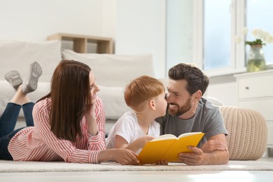 Photo of Happy parents with their child reading book on floor at home