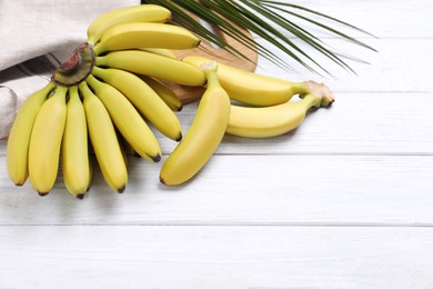 Photo of Tasty ripe baby bananas on white wooden table. Space for text