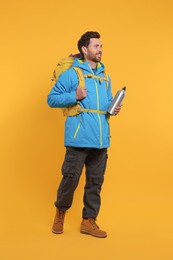 Photo of Happy man with backpack and thermo bottle on orange background. Active tourism
