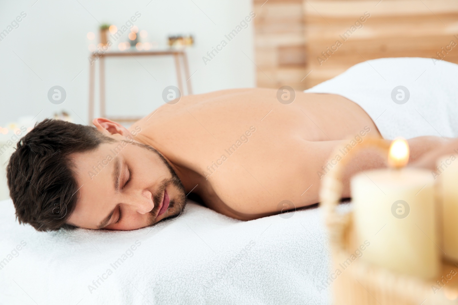 Photo of Handsome man relaxing on massage table in spa salon