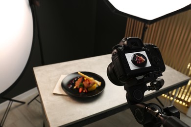 Photo of Professional camera with picture of baked chicken, parsnip and strawberries on white table in photo studio. Food photography