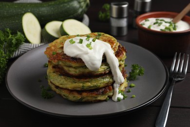 Delicious zucchini fritters with sour cream on wooden table