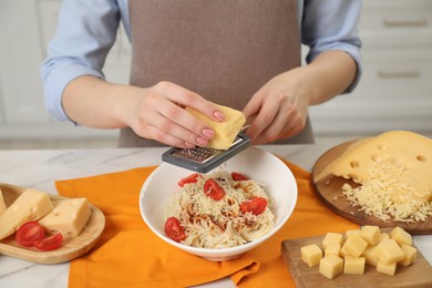 Photo of Woman grating cheese onto delicious pasta at white marble table indoors, closeup