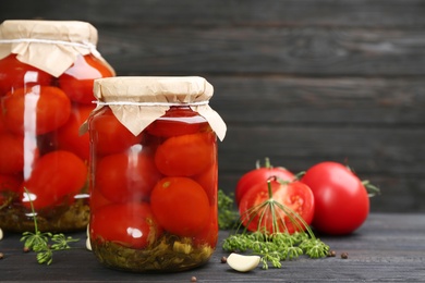 Glass jars of pickled tomatoes on black wooden table. Space for text