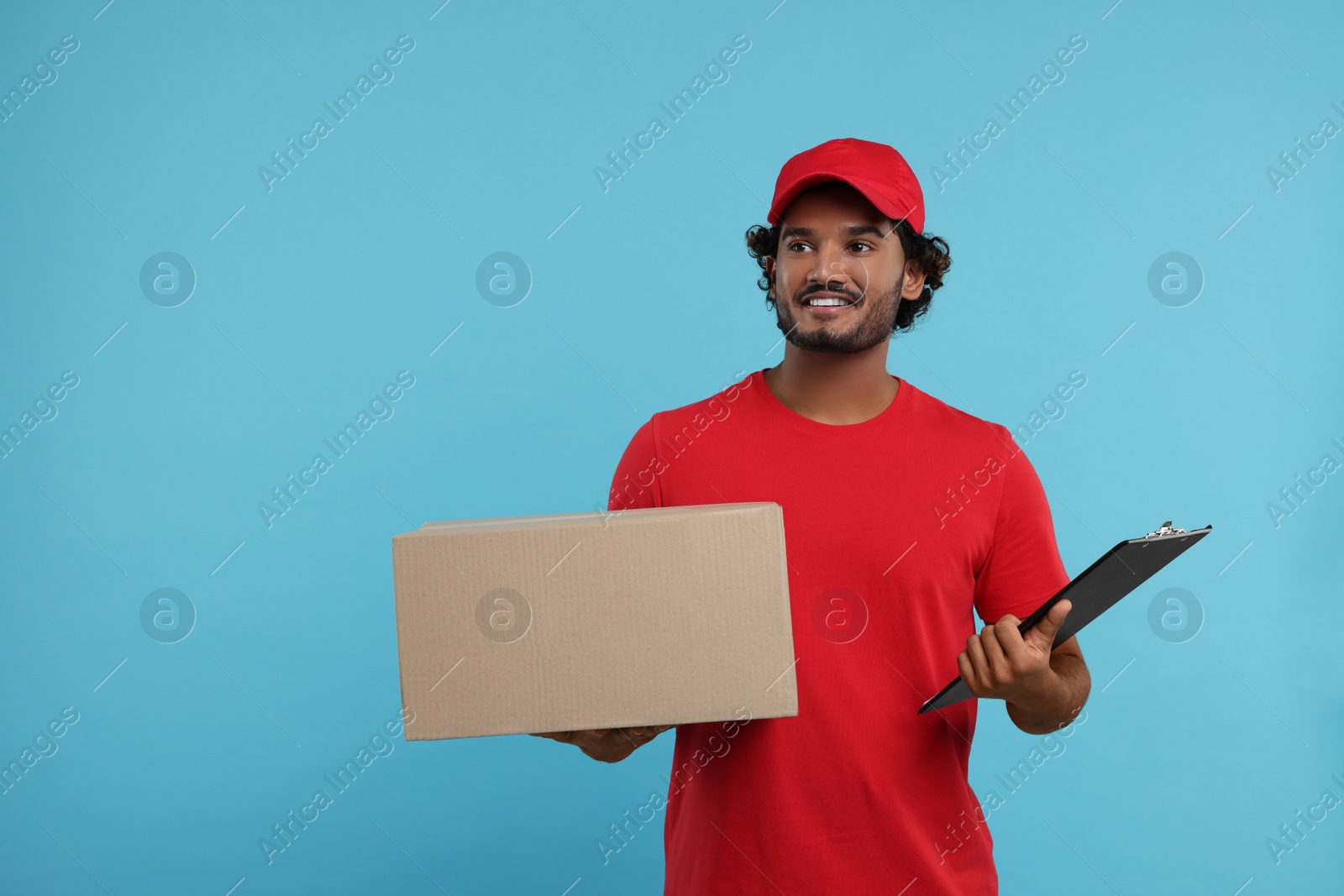 Photo of Happy courier with parcel and clipboard on light blue background, space for text