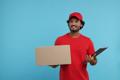 Photo of Happy courier with parcel and clipboard on light blue background, space for text