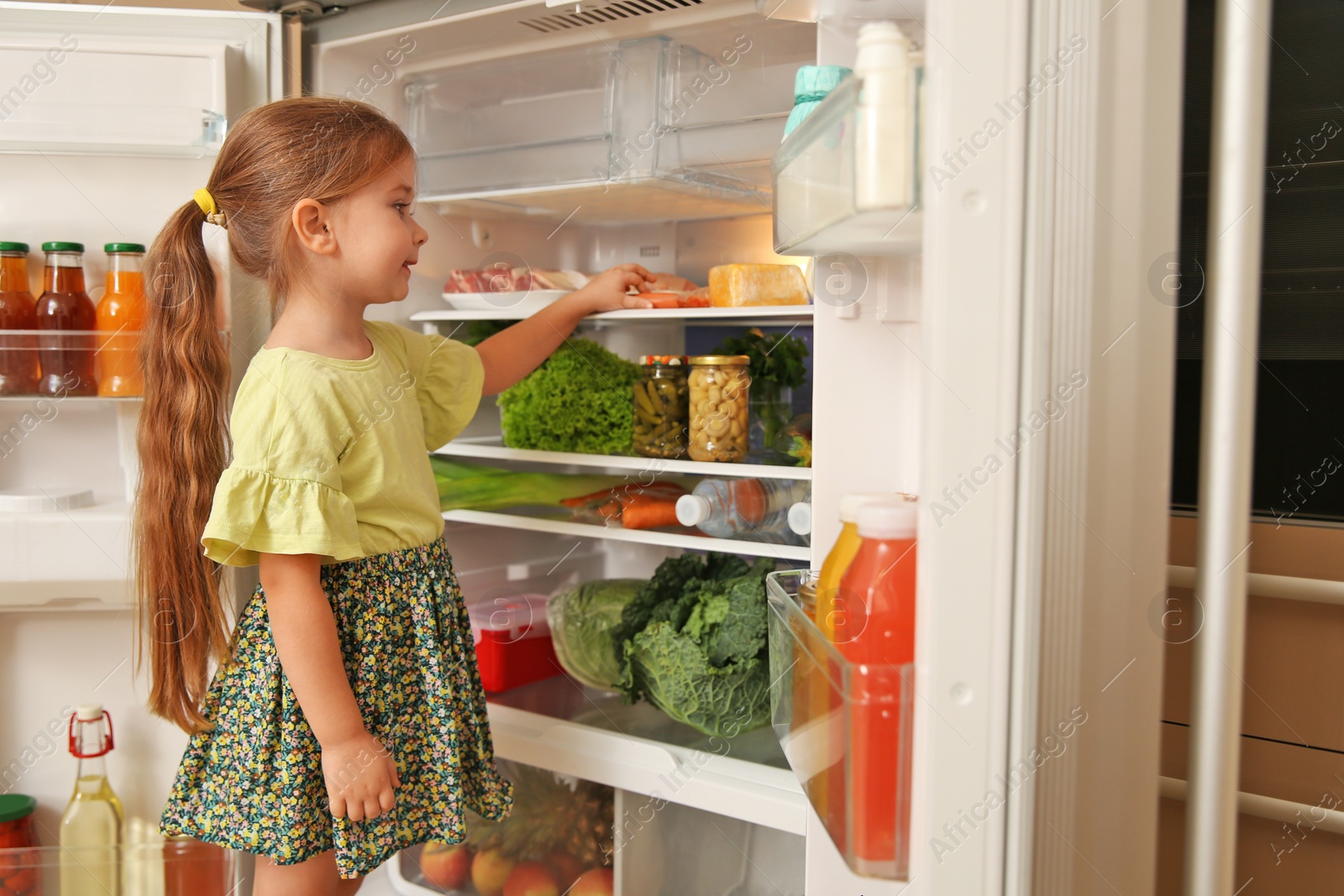 Photo of Cute little girl choosing food in refrigerator at home