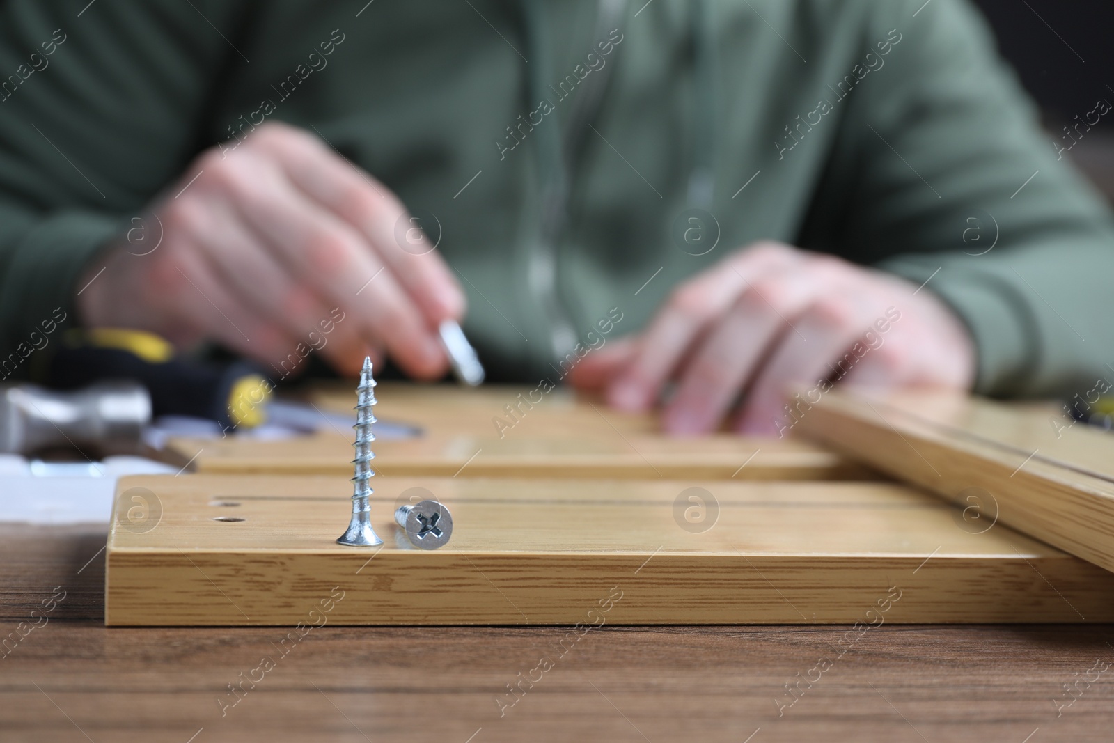 Photo of Man assembling wooden furniture at table, focus on fasteners