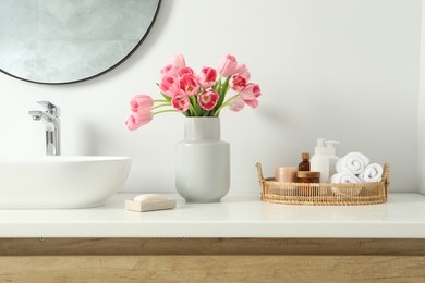 Vase with beautiful pink tulips and toiletries near sink in bathroom