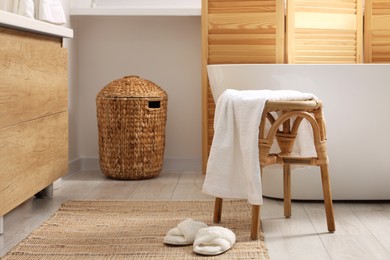 Photo of Wicker stool with towel and slippers on rug in bathroom