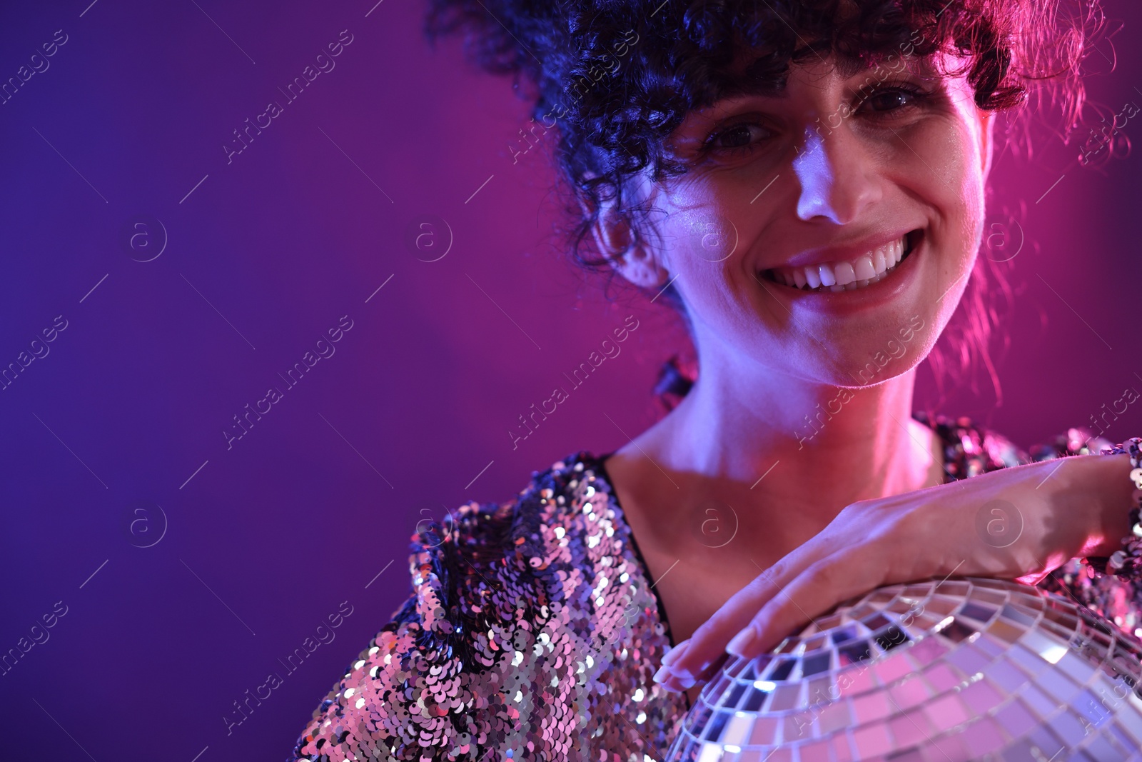 Photo of Beautiful young woman with disco ball posing on color background in neon lights, closeup. Space for text