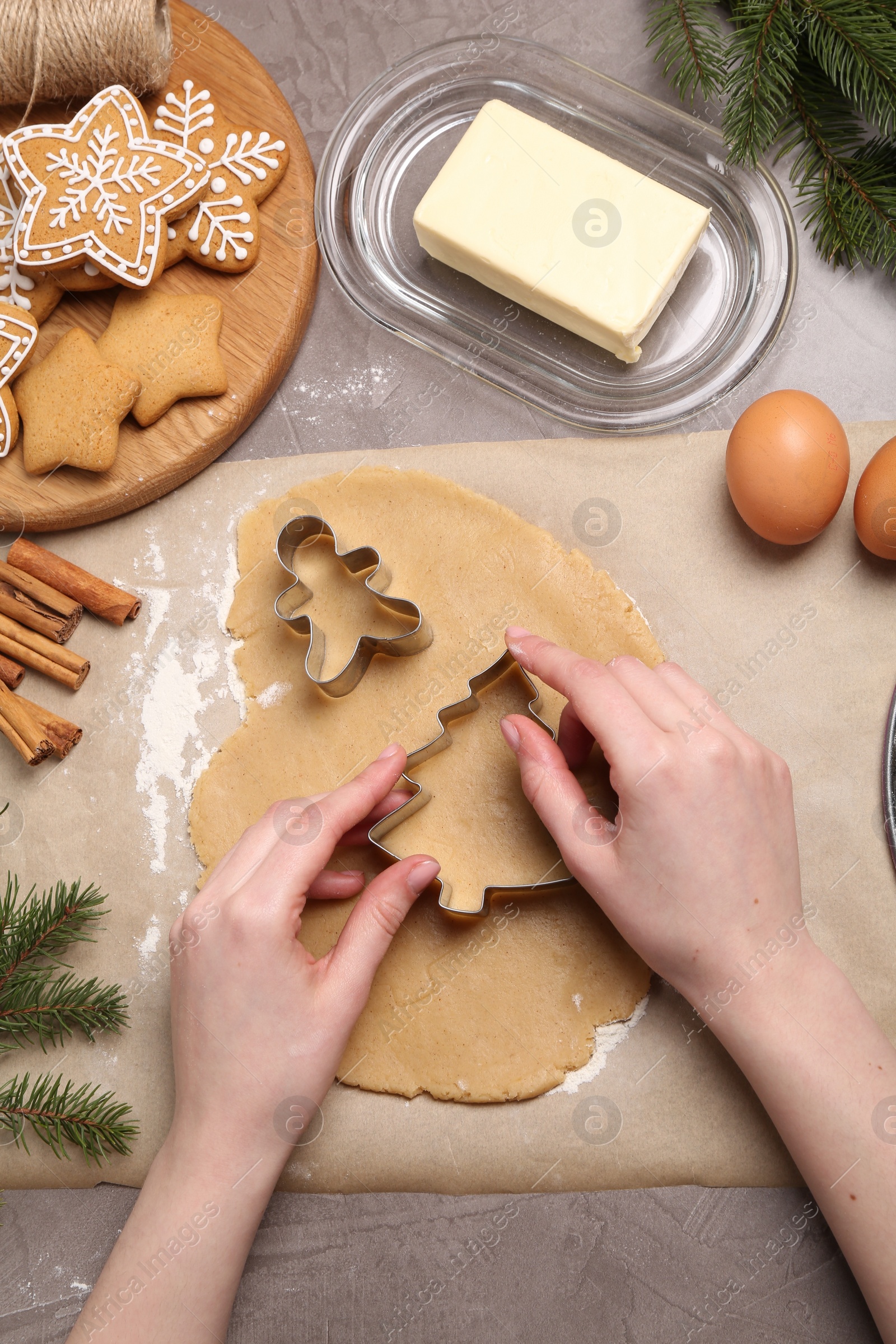 Photo of Woman making Christmas cookies with cutters at grey table, top view