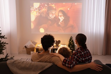 Photo of Family watching Christmas movie via video projector at home, back view