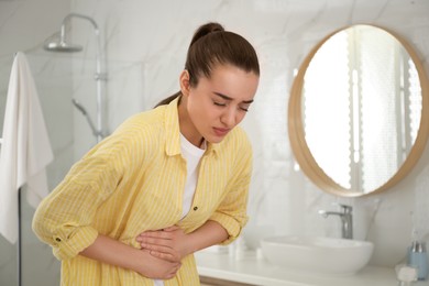 Photo of Young woman suffering from stomach ache in bathroom. Food poisoning