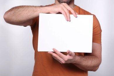 Man holding sheet of paper on light grey background, closeup. Mockup for design