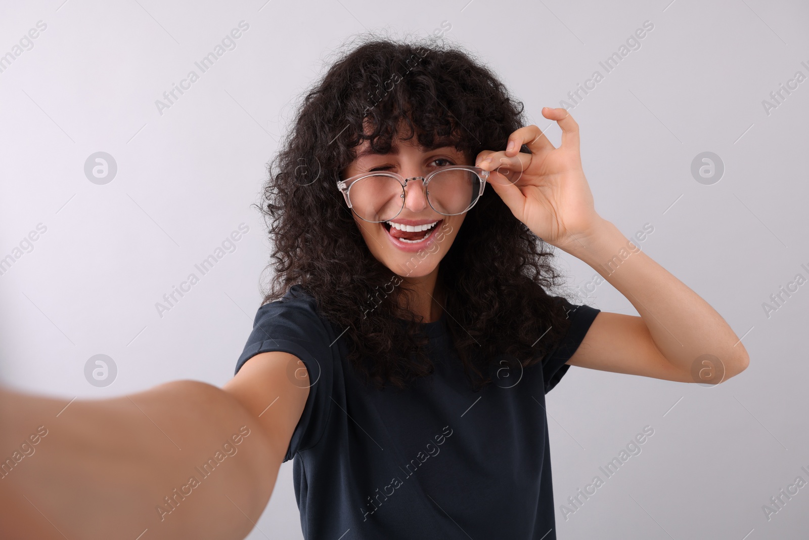Photo of Beautiful young woman in eyeglasses taking selfie on light grey background
