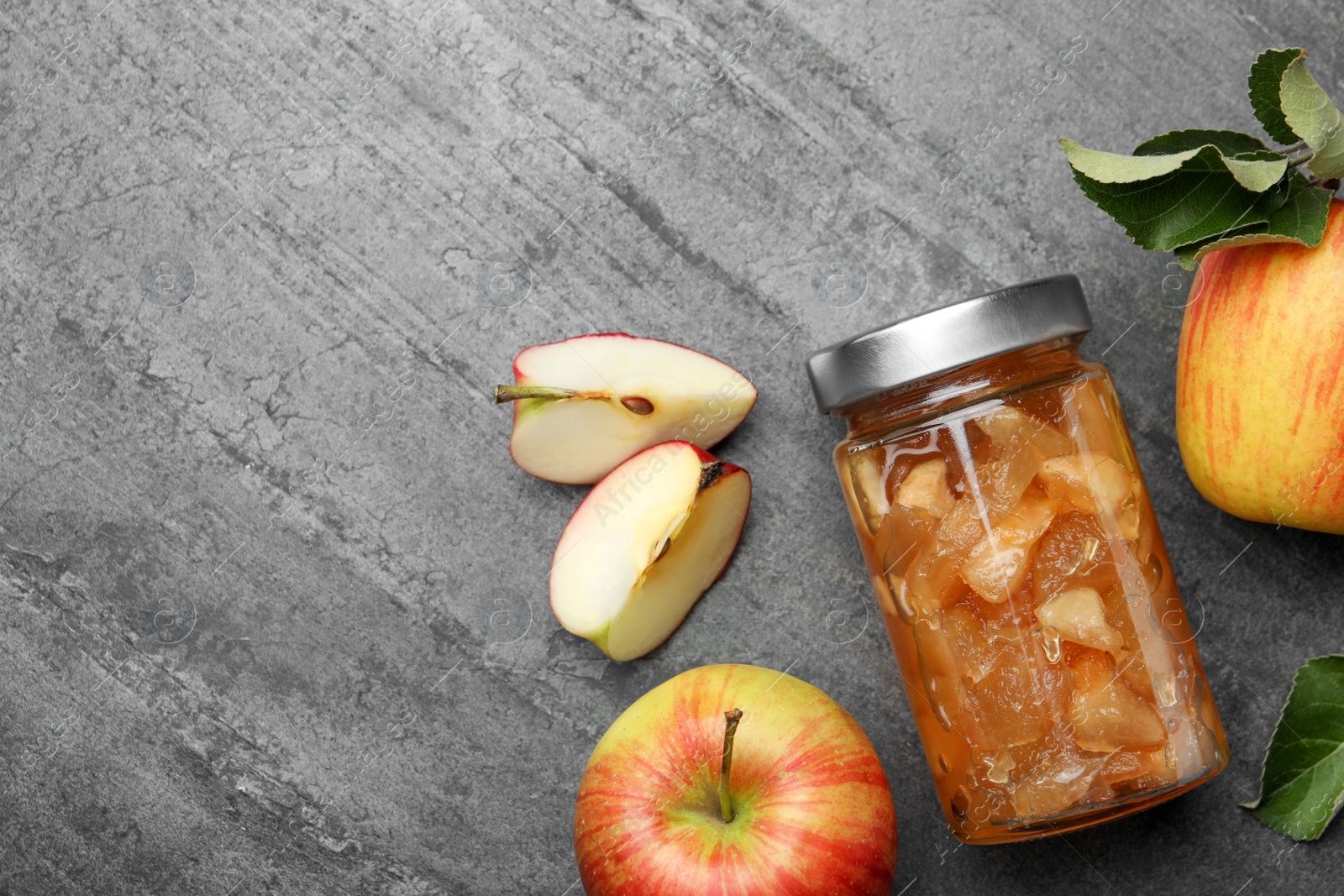 Photo of Tasty apple jam in glass jar and fresh fruits on grey table, flat lay. Space for text