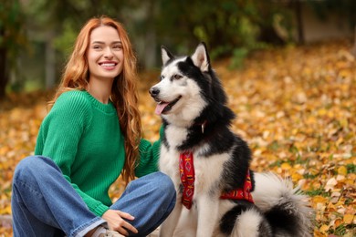 Photo of Happy woman with cute Siberian Husky sitting in autumn park