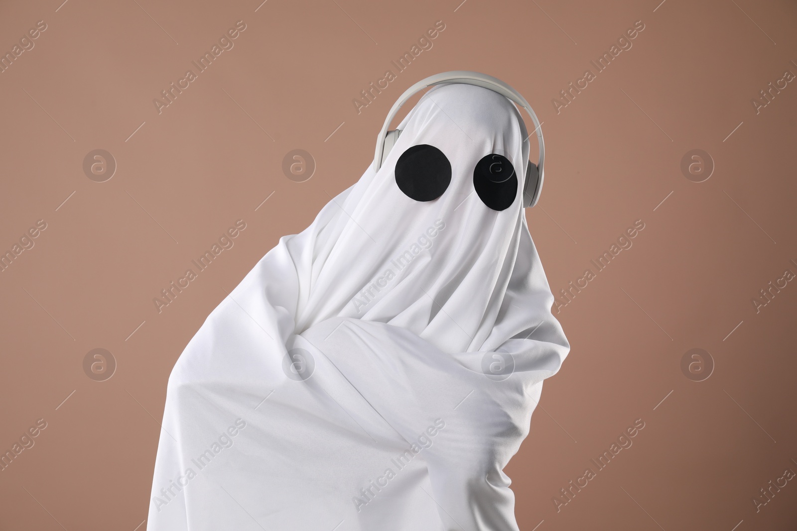 Photo of Person in ghost costume wearing headphones on dark beige background