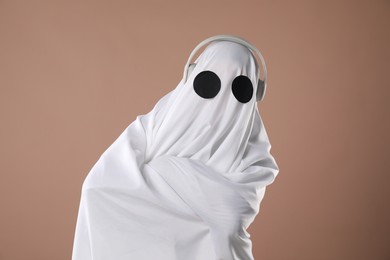 Person in ghost costume wearing headphones on dark beige background