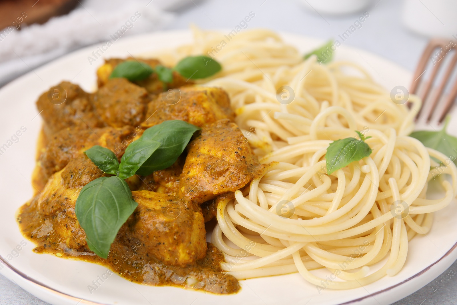 Photo of Delicious chicken, pasta with curry sauce and basil on plate, closeup