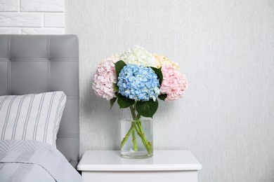 Photo of Beautiful hydrangea flowers in vase on white bedside table indoors