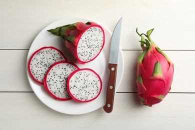 Photo of Plate of delicious cut and whole pitahaya fruits with knife on white wooden table, flat lay