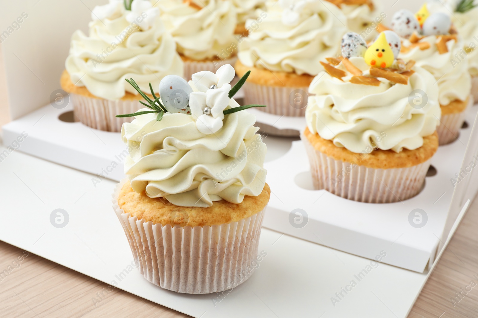 Photo of Tasty Easter cupcakes in box on wooden table, closeup