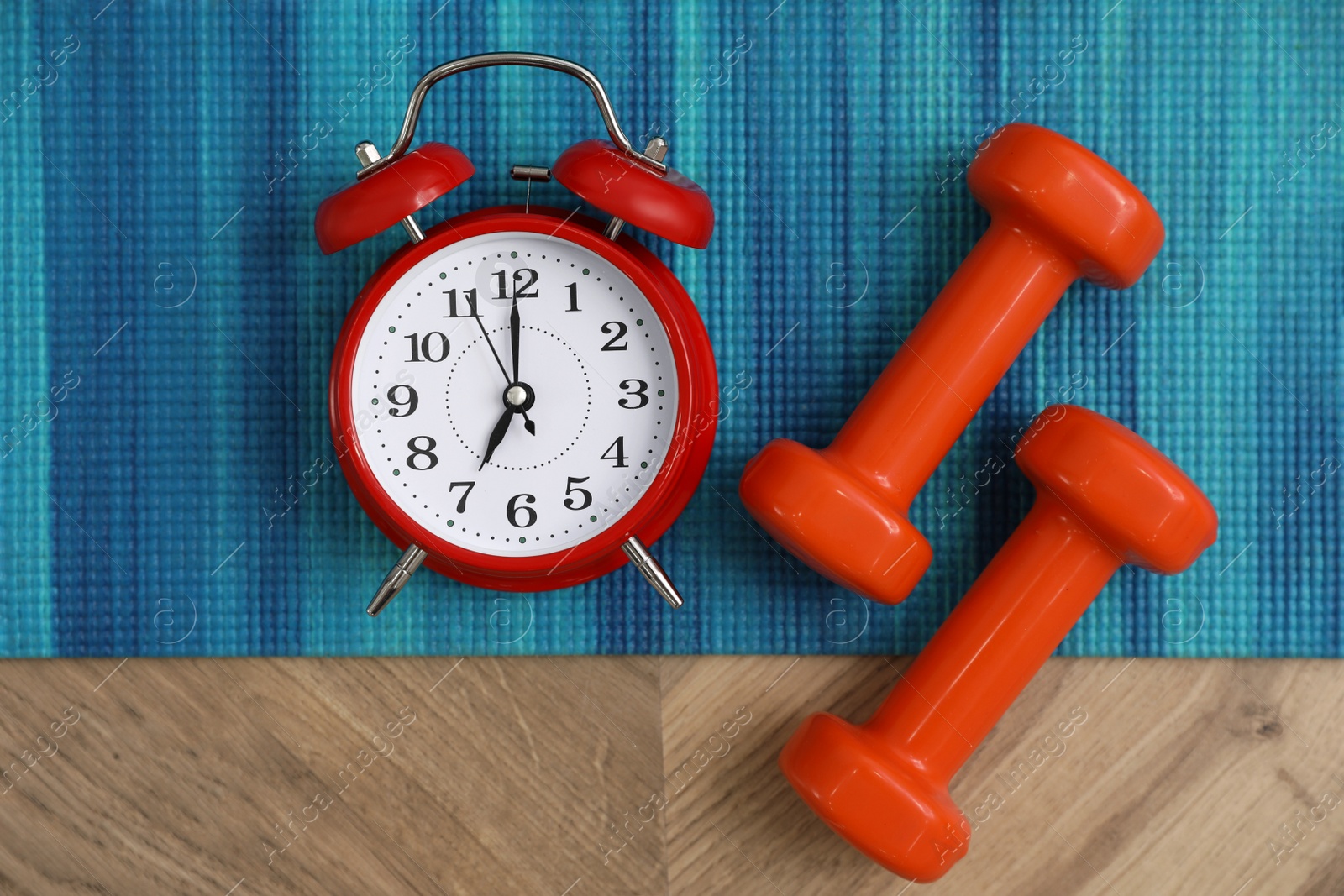 Photo of Alarm clock, yoga mat and dumbbells on wooden background, flat lay. Morning exercise