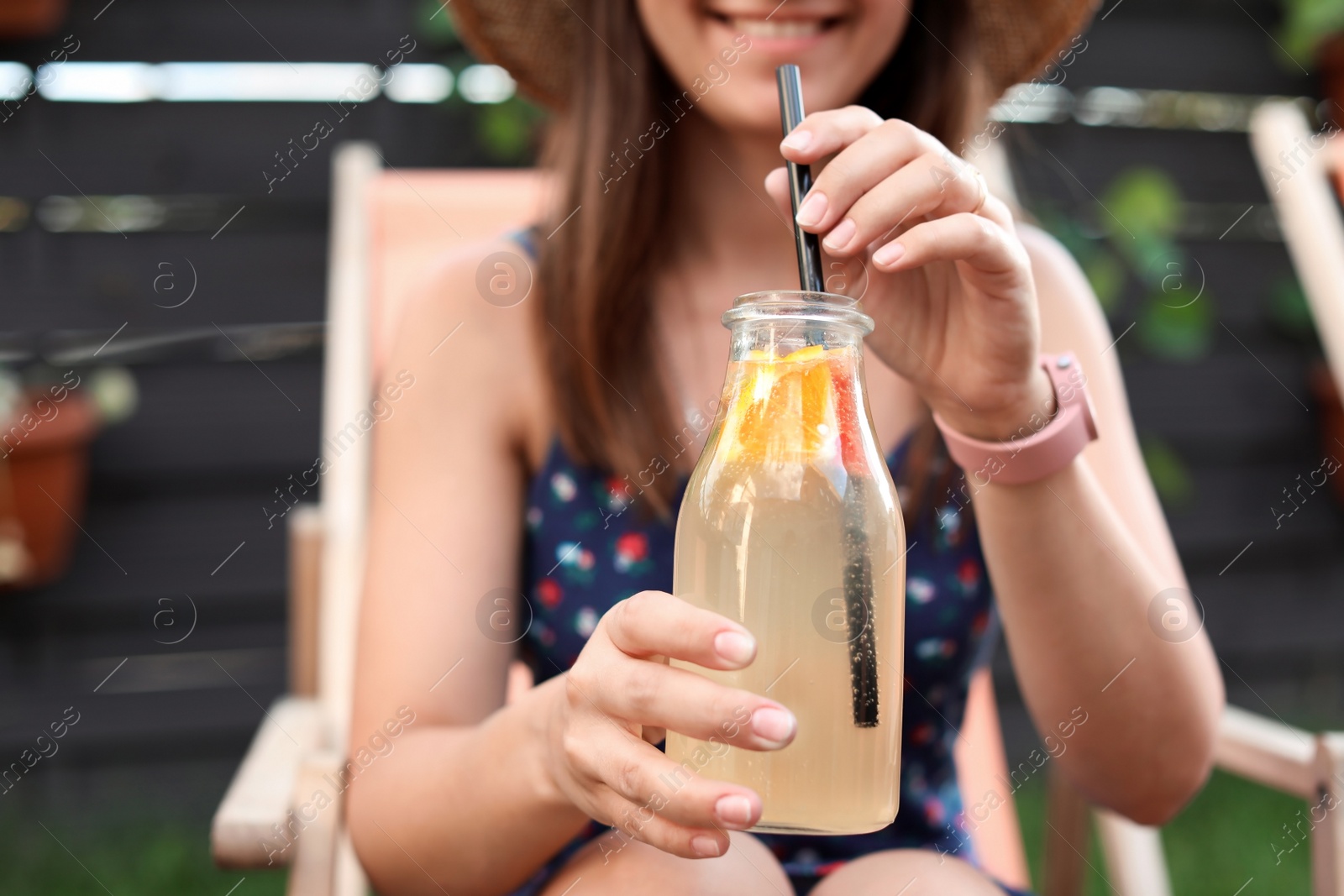 Photo of Young woman with bottle of tasty lemonade outdoors, closeup