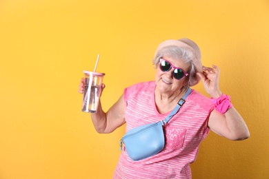 Portrait of cool grandmother with drink on color background, space for text