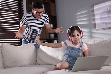 Photo of Internet addiction. Man scolding his daughter while she using laptop in living room
