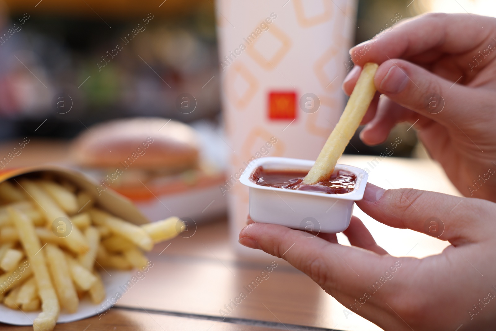 Photo of Lviv, Ukraine - September 26, 2023: Woman dipping McDonald's french fry into sauce at wooden table outdoors, closeup