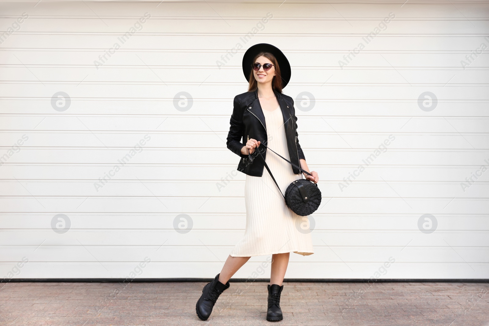 Photo of Beautiful young woman with stylish handbag near white wall outdoors