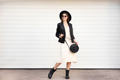 Beautiful young woman with stylish handbag near white wall outdoors