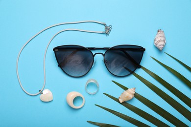 Photo of Stylish sunglasses, seashells and accessories on light blue background, flat lay