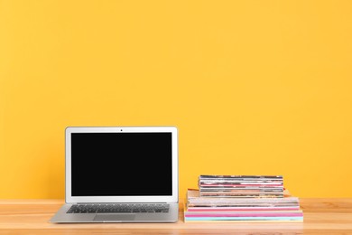 Laptop and stack of magazines on wooden table. Space for text